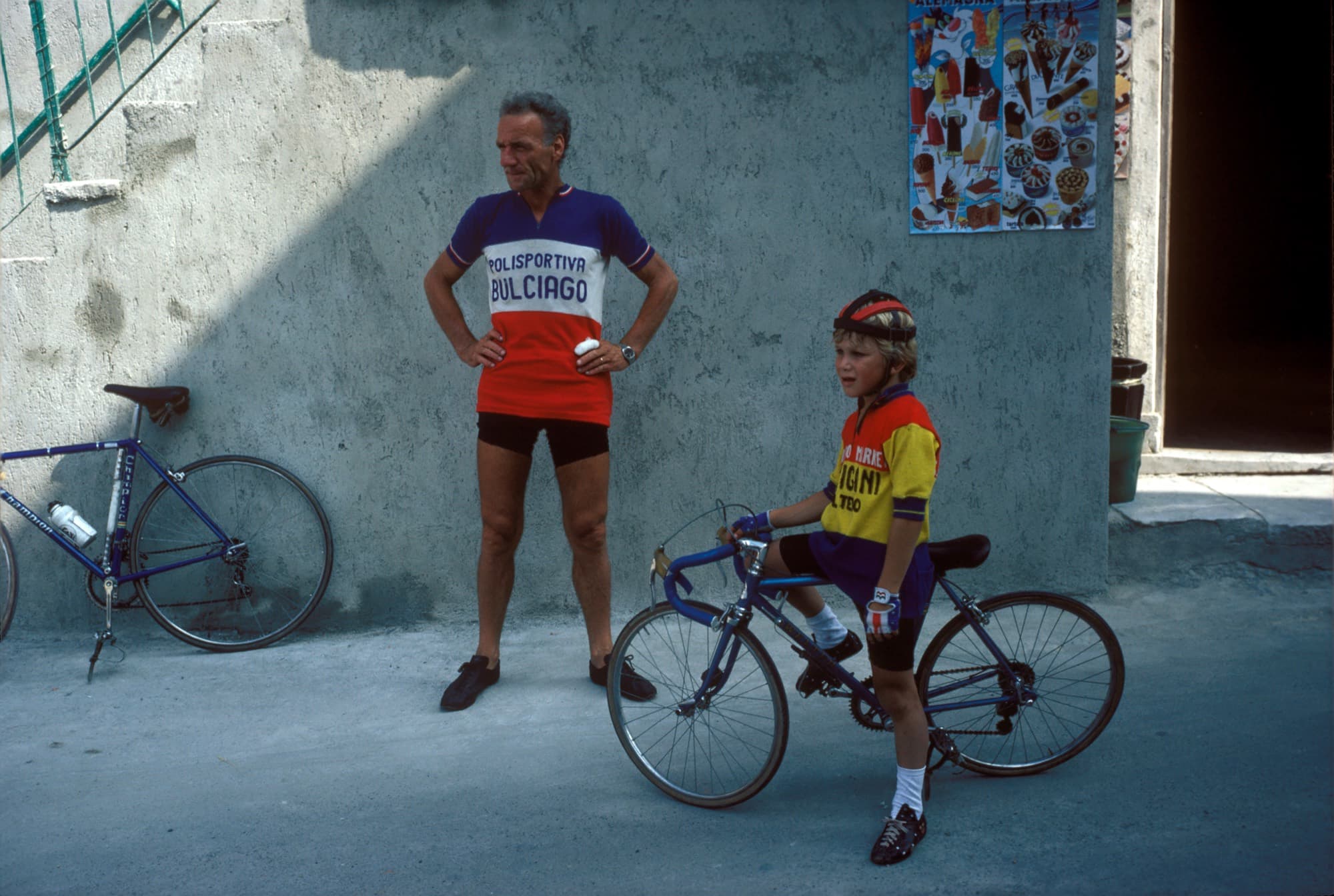 Two club cyclists in Polisportiva Bulciago kit resting against a painted wall